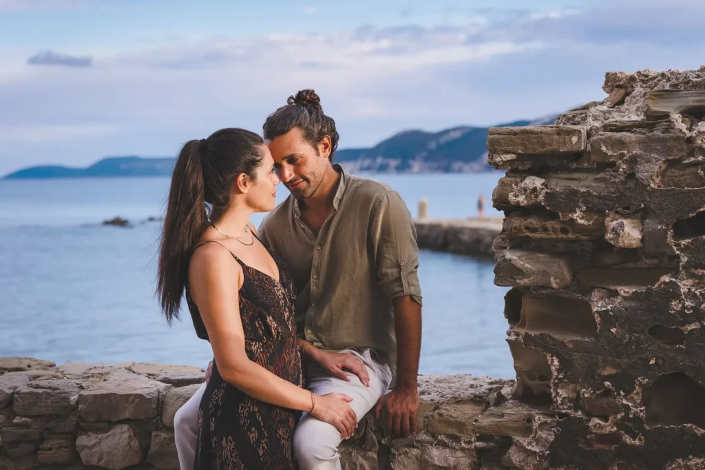 a man and woman sitting on a stone ledge by water